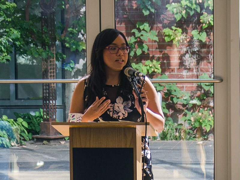 Photo of Frances Gonzalez gesturing at a podium and speaking into the built-in mic