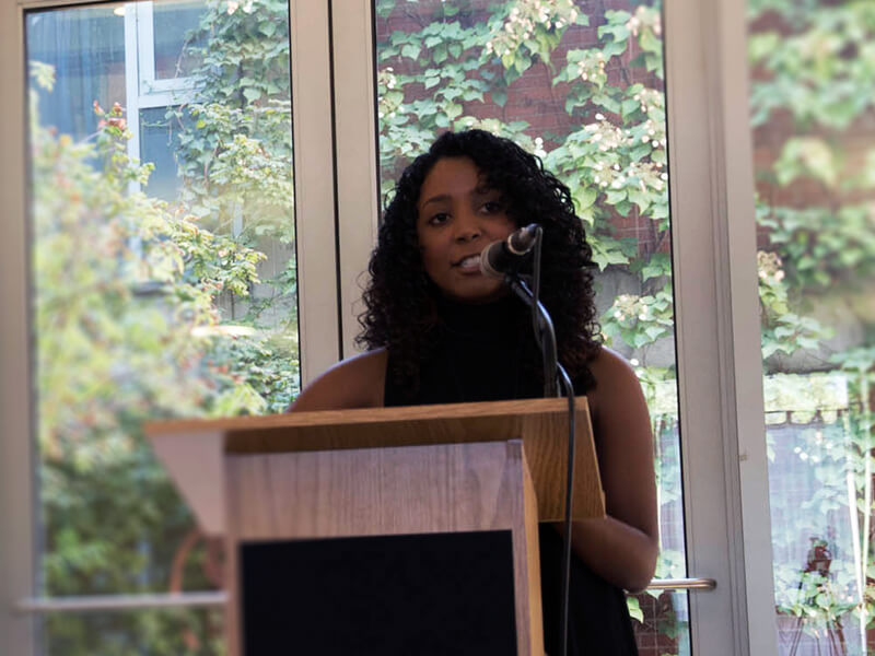 Photo of Jazmyn Latimer standing behind a podium and speaking into built-in mic