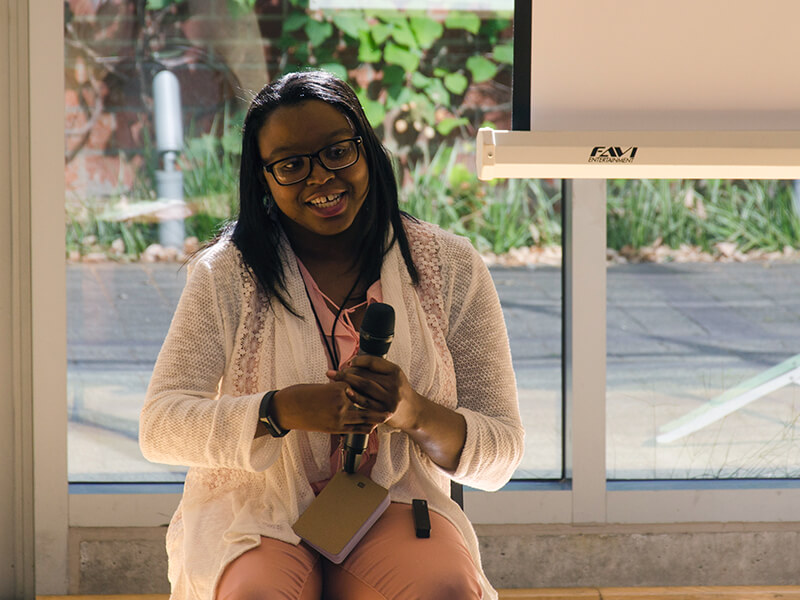 Photo of Keah Brown sitting and smiling while holding a mic
